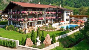 A multi-story hotel with balconies adorned with flowers, a swimming pool, and a mountainous backdrop. - (21) Two-room vacation apartment 50 sqm, bathroom/WC, kitchen, balcony (Reit im Winkl)