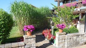 A pathway flanked by lush greenery and potted flowers leading to a building with balconies. - (21) Two-room vacation apartment 50 sqm, bathroom/WC, kitchen, balcony (Reit im Winkl)