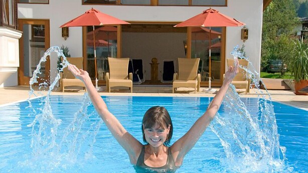 A swimming pool with a person raising their arms, surrounded by lounge chairs and umbrellas. - (21) Two-room vacation apartment 50 sqm, bathroom/WC, kitchen, balcony (Reit im Winkl)