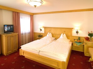 A hotel room with a double bed, wooden headboard, two bedside tables with lamps, a television on a cabinet, and a floral carpet. - (21) Two-room vacation apartment 50 sqm, bathroom/WC, kitchen, balcony (Reit im Winkl)