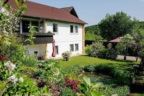 Una casa a due piani con un giardino, uno stagno e un edificio con tetto rosso.