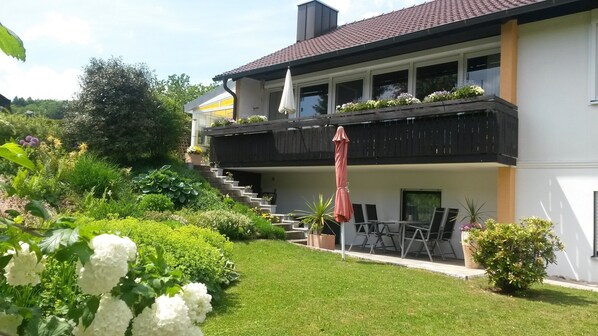 Una casa a due piani con un balcone, una scala e un giardino pieno di piante e fiori.