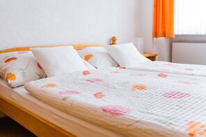 Ein Bett mit einer blumengemusterten Tagesdecke, einem Holzkopfstück und zwei Kissen mit Blumenmotiven.
