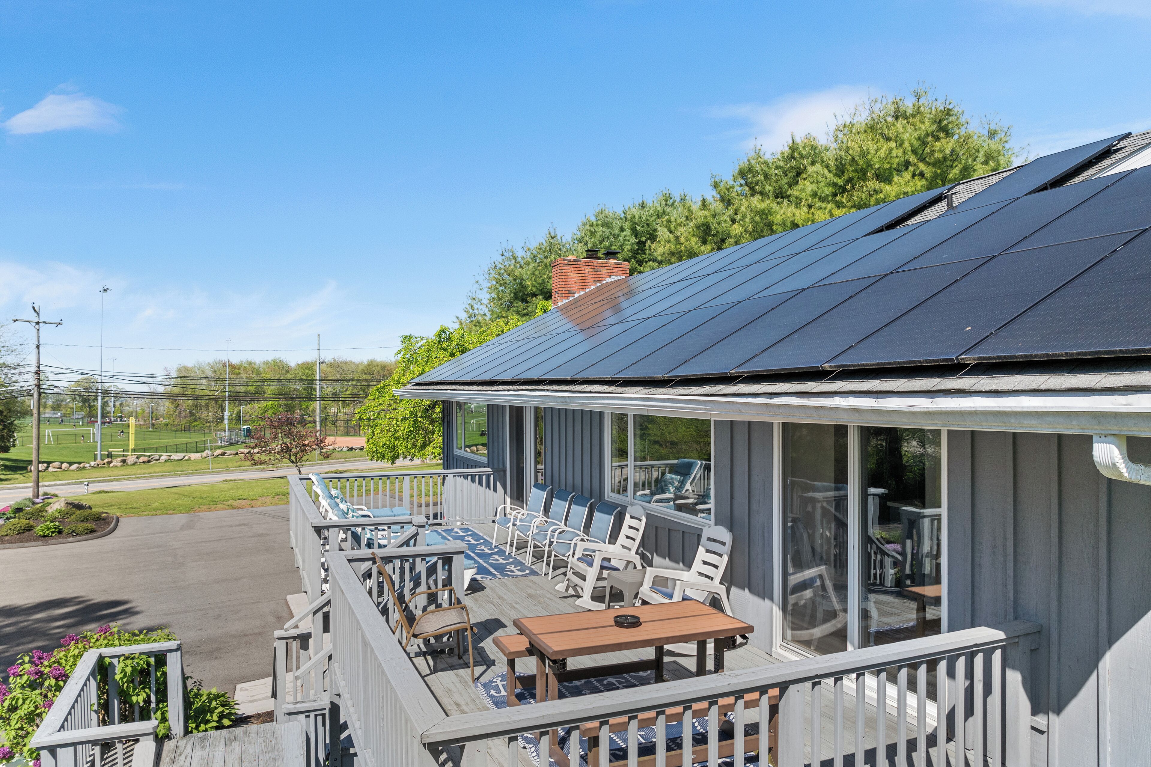 A covered outdoor seating area with tables and chairs, a wooden deck, and a view of the surrounding landscape.