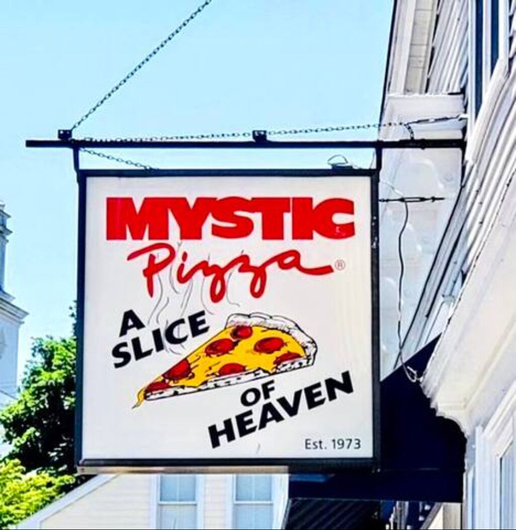 A sign for Mystic Pizza, established in 1973, hanging outside a building.