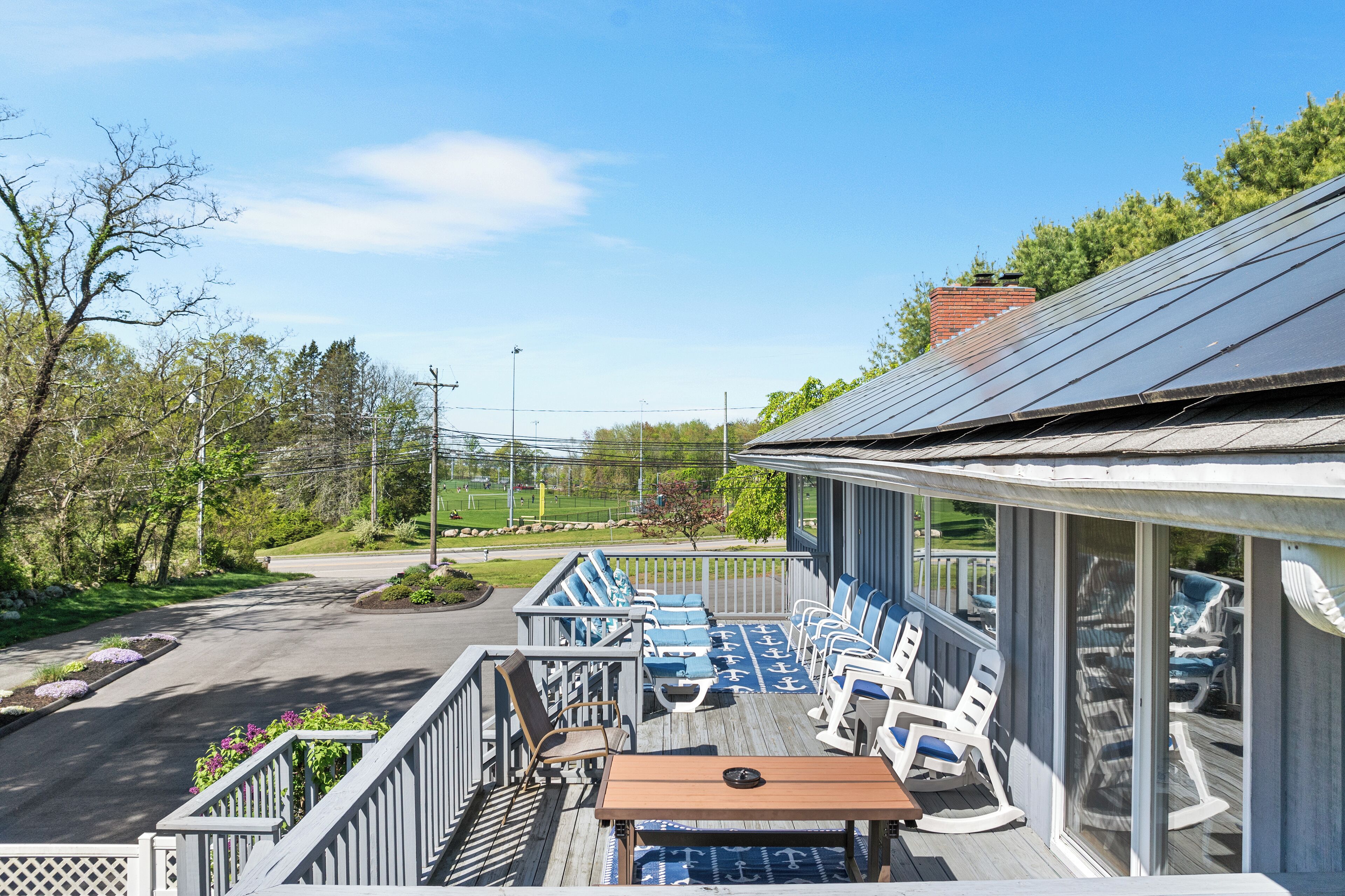 A deck with outdoor seating, a table, and a view of a road and greenery.