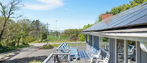 A deck with outdoor seating, a table, and a view of a road and greenery.