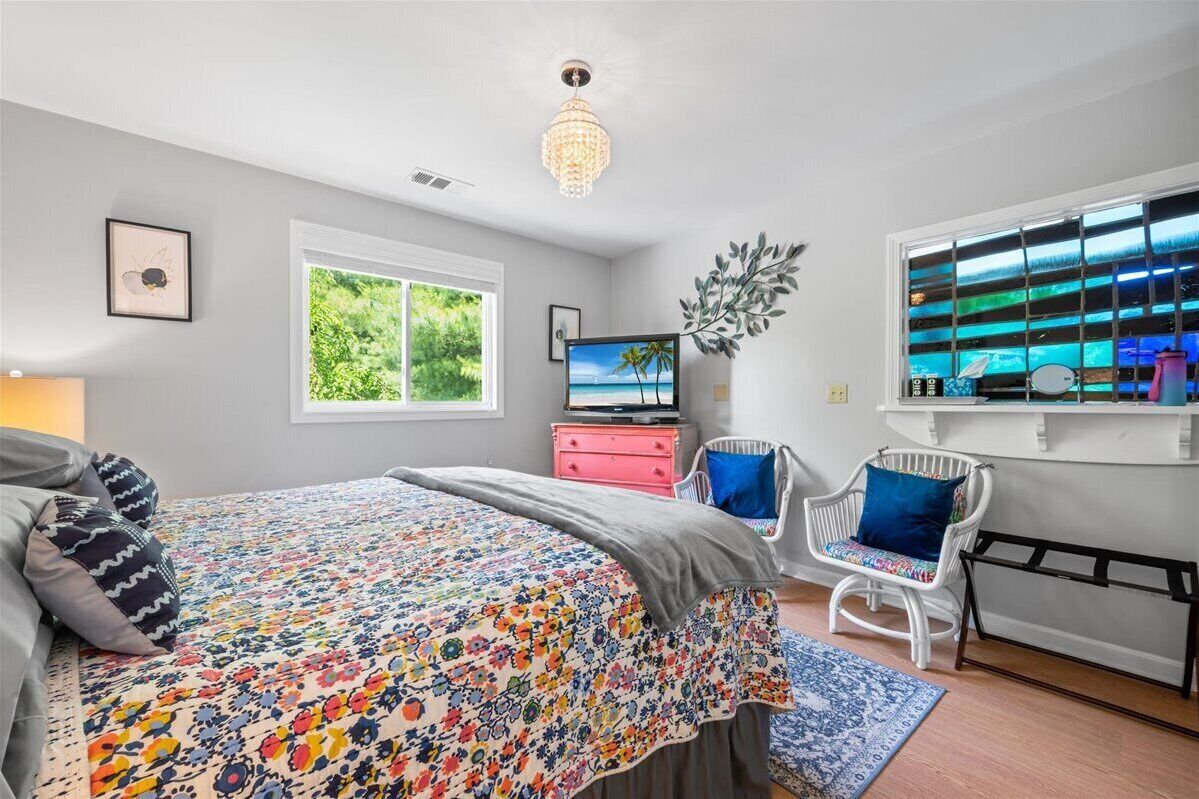 Un dormitorio con cama, televisión, ventana con vistas, candelabro y una silla.