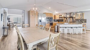 Una cocina moderna con una isla grande, electrodomésticos de acero inoxidable y un comedor con mesa y sillas de madera.