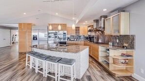 Una cocina moderna con una isla central, taburetes de bar, armarios de madera, electrodomésticos de acero inoxidable e iluminación colgante.