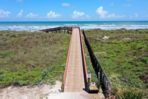 Ein hölzerner Steg führt zu einem Strand, mit einem Stoppschild und einem Schild, das einen überwachten Bereich kennzeichnet.