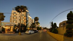 A multi-story hotel with a central entrance, palm trees, and a street view. - Guest House Amman (Amman)