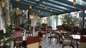 A restaurant with a covered patio area, featuring patterned tile flooring, wooden tables and chairs, hanging pendant lights, and potted plants. - Guest House Amman (Amman)