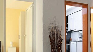 A hallway with a white door leading to a bathroom, a vase with branches, and a kitchen area visible through an open door. - Raya Maisonette (Sofia)
