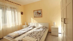 A bedroom with a bed, two bedside tables, a nightstand, a window with sheer curtains, a painting on the wall, and a wardrobe. - Raya Maisonette (Sofia)