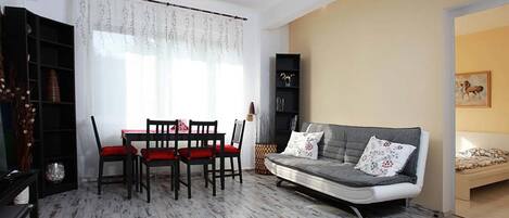 Una sala de estar con una mesa de comedor, cuatro sillas, un sofá y una estantería.
