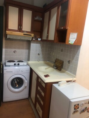 A compact kitchen with a washing machine, a sink, and wooden cabinets. - Times Apart (Cesme)
