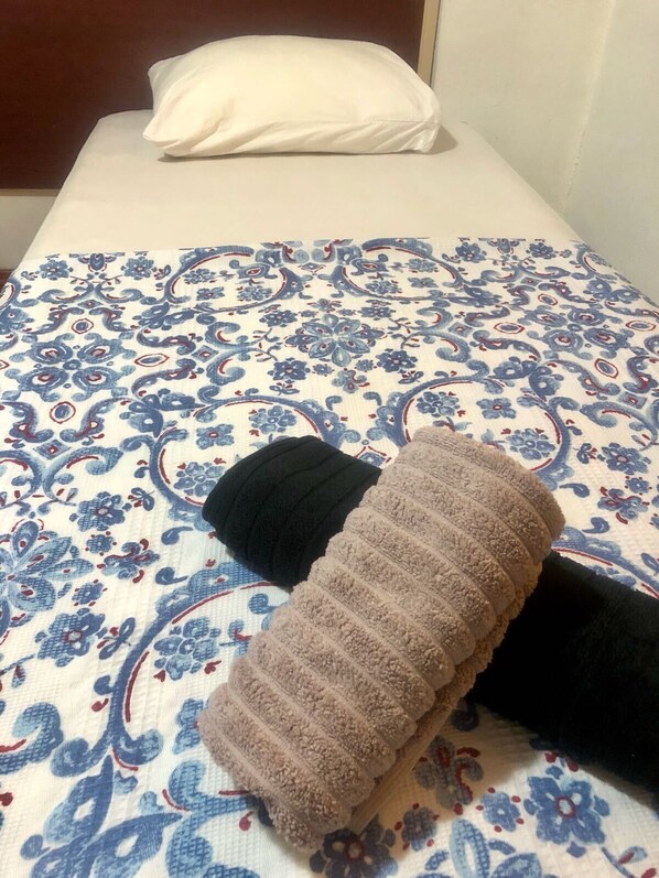 A bed with a patterned bedspread, a white pillow, and two rolled-up towels. - Times Apart (Cesme)