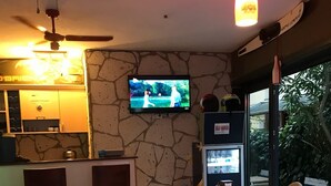 Un restaurante con pared de piedra, un televisor sobre una barra y mesas con manteles a cuadros.