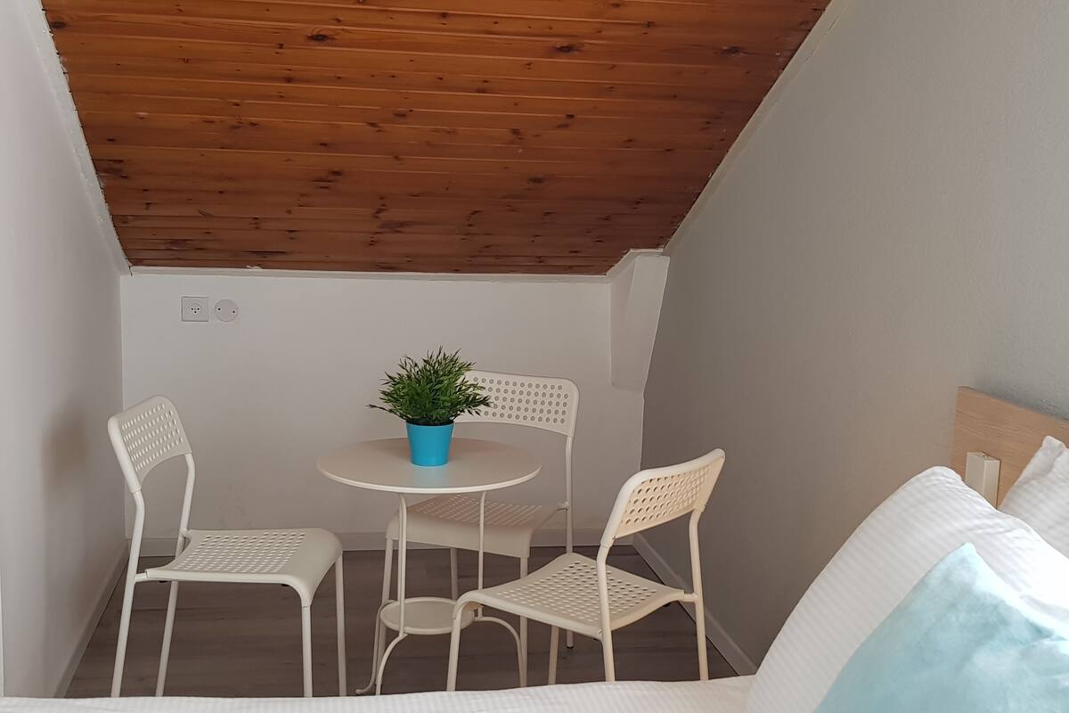 A small, enclosed balcony with a wooden ceiling, white furniture, and a potted plant.