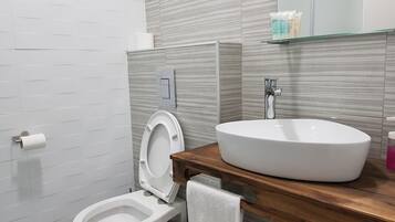 Et moderne badeværelse med toilet, bidet og en stor vask med et spejl over.