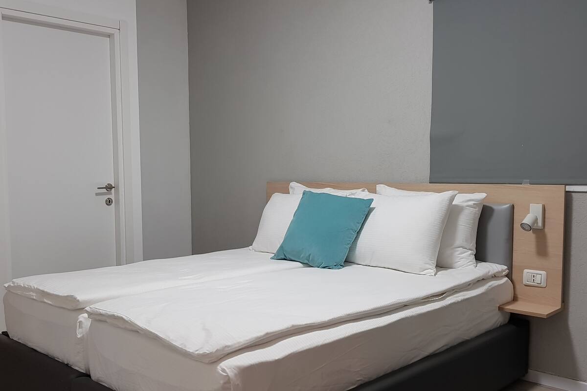 A neatly made bed with white bedding and a single teal pillow, a wooden headboard, and a white door to the left.