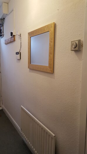 A hallway with a radiator, a wall-mounted thermostat, and a framed mirror with a textured frame. - Stunning Somerset House (Middlesbrough)