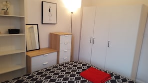 Ein Schlafzimmer mit einem Bett, einem Kleiderschrank, einem Schminktisch und einem Spiegel, sowie einem gerahmten Bild an der Wand.