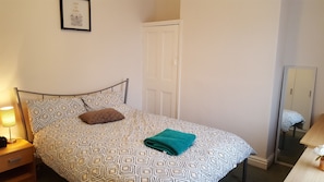 A bedroom with a patterned bedspread, a single pillow, a folded towel, a bedside lamp, and a wardrobe with a mirror. - Stunning Somerset House (Middlesbrough)