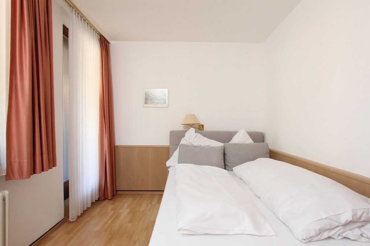 Ein Hotelzimmer mit Bett, Nachttisch, Lampe und einem Vorhangfenster.