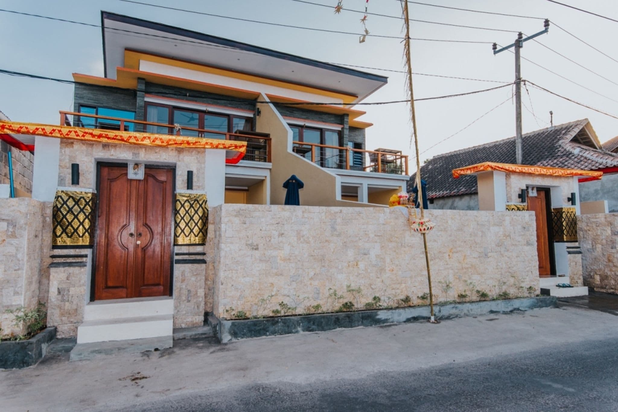 A modern two-story house with a prominent wooden door, a balcony, and a stone wall.