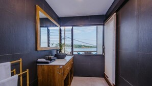 A modern bathroom with a large mirror, dark walls, a wooden vanity, and a view of the outdoors through a window. - Secret Outlook Lembongan (Lembongan Island)
