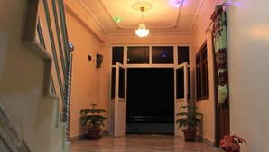 A hallway with a marble floor, two potted plants, a chandelier, and a door leading to a balcony. - Natures Treat Homestay (Tansen)