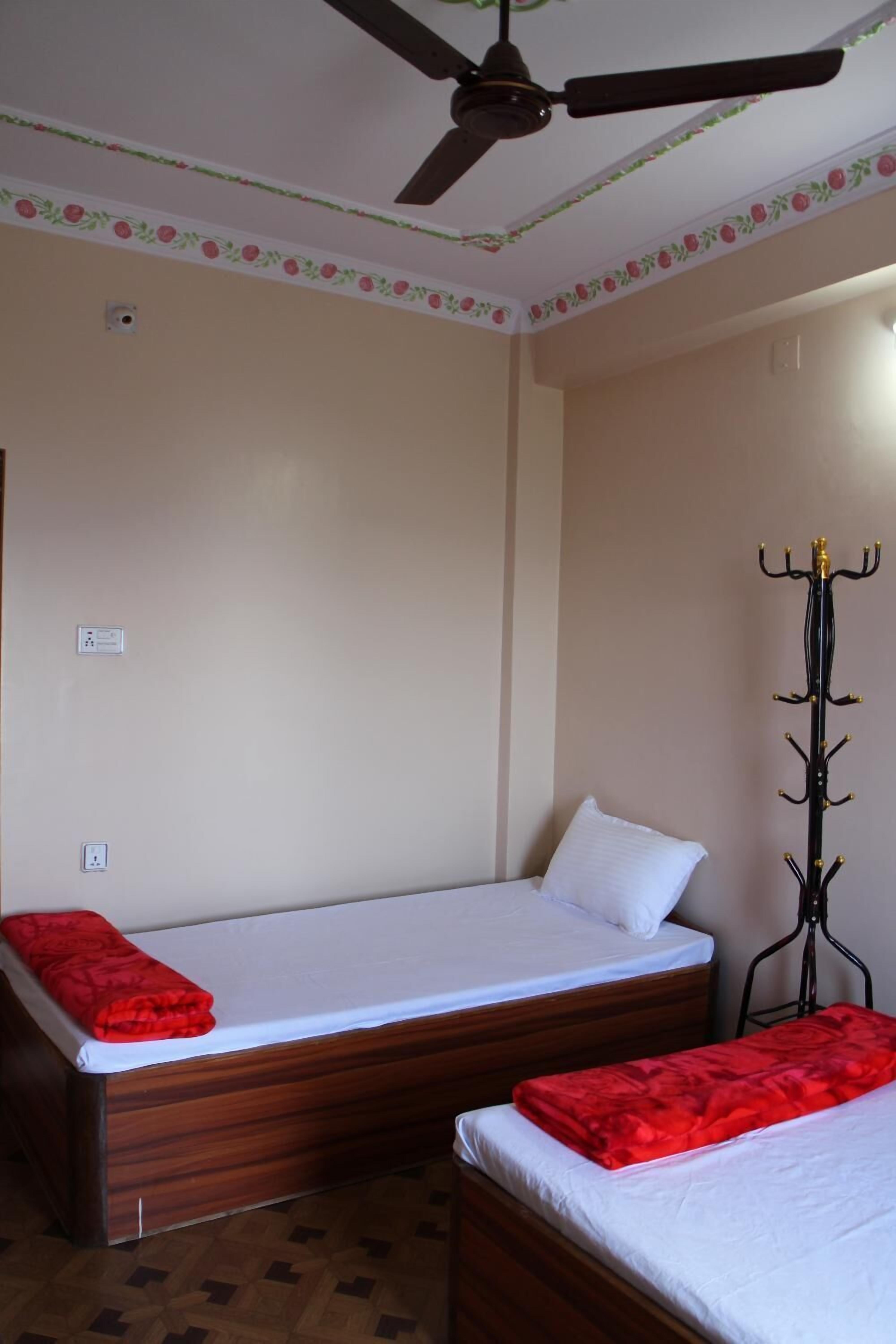A single bed with a red blanket, a ceiling fan, and a coat rack.
