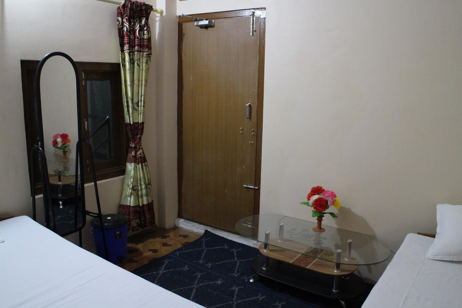 Un dormitorio con cama, espejo, armario, una mesita con un jarrón y una mesa de vidrio con un jarrón.