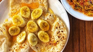 A plate of crepes with banana slices and syrup, a bowl of vegetable fritters, and a cup of black coffee on a wooden table. - Natures Treat Homestay (Tansen)
