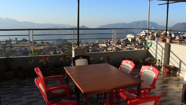 A terrace with a wooden table and red chairs, overlooking a cityscape and mountains. - Natures Treat Homestay (Tansen)