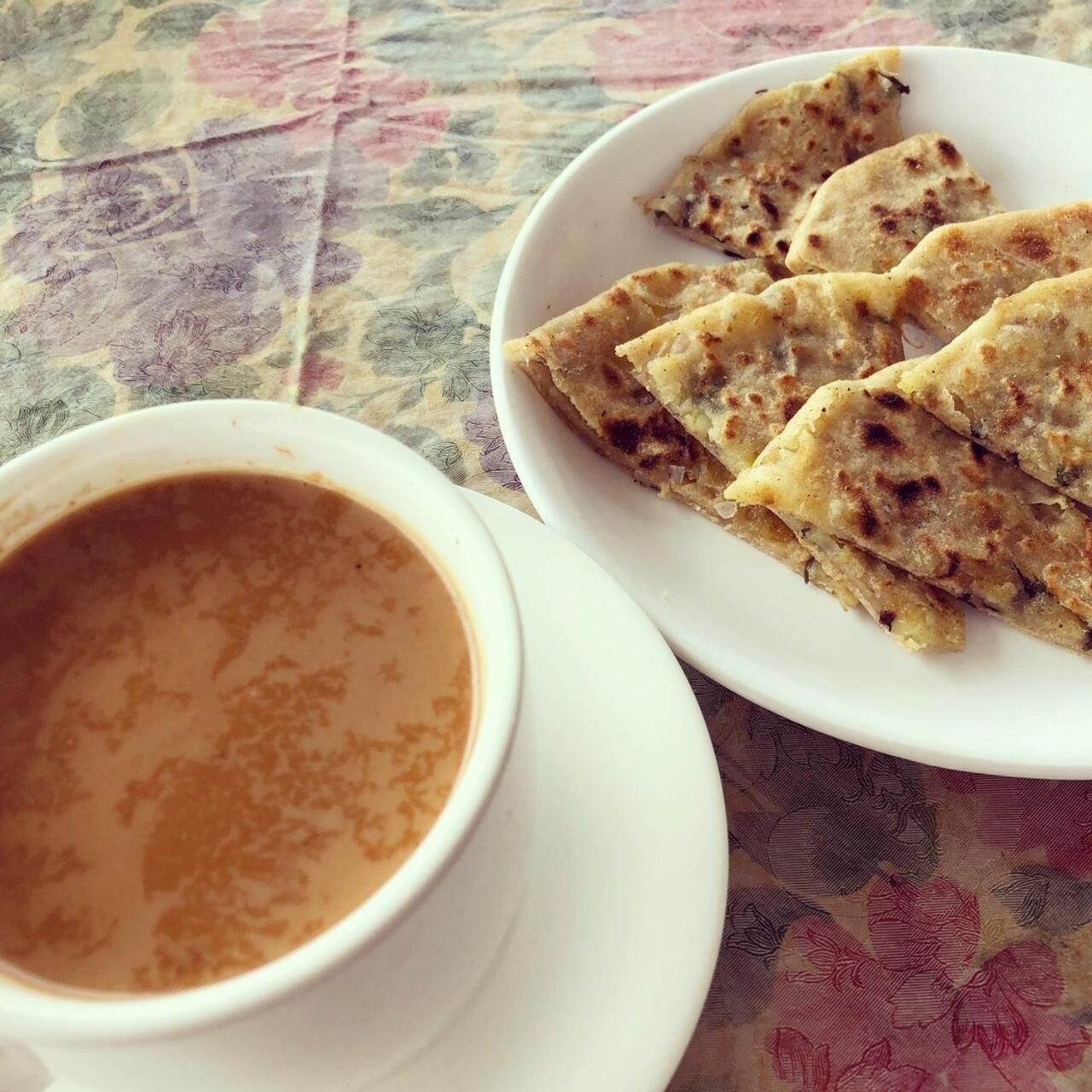 Un plato de pan plano y una taza de té sobre una mesa con mantel floreado.