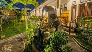 A well-maintained garden with a fountain, palm trees, and a pathway leading to a building with multiple doors. - Kastapar Bridge Guest House (Lembongan Island)