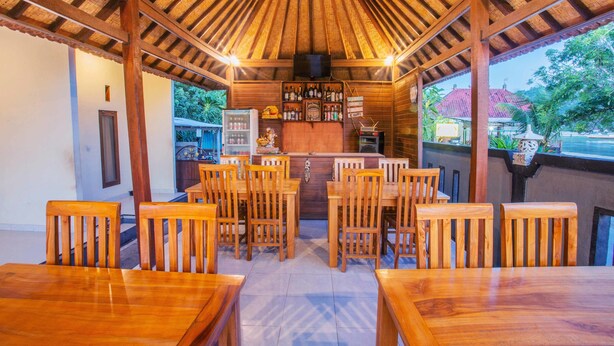 A wooden bar area with multiple chairs and tables, a refrigerator, and a shelf with bottles. - Kastapar Bridge Guest House (Lembongan Island)