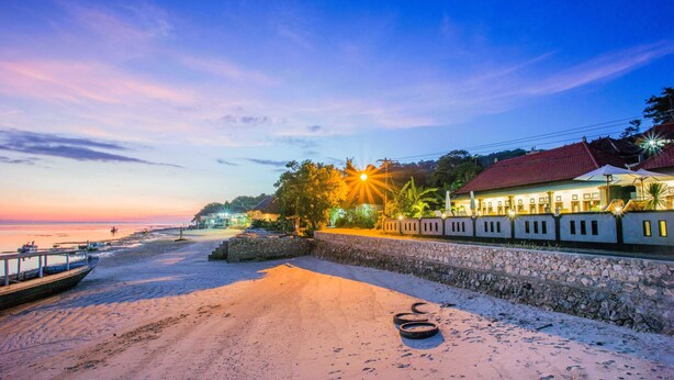 A beachside hotel with a stone wall, a boat dock, and a sunset view. - Kastapar Bridge Guest House (Lembongan Island)