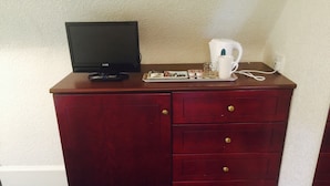 A wooden cabinet with a flat-screen TV, remote control, a white mug, a glass, and a tray with snacks. - Brentwood Villa Bed and Breakfast (Aberdeen)