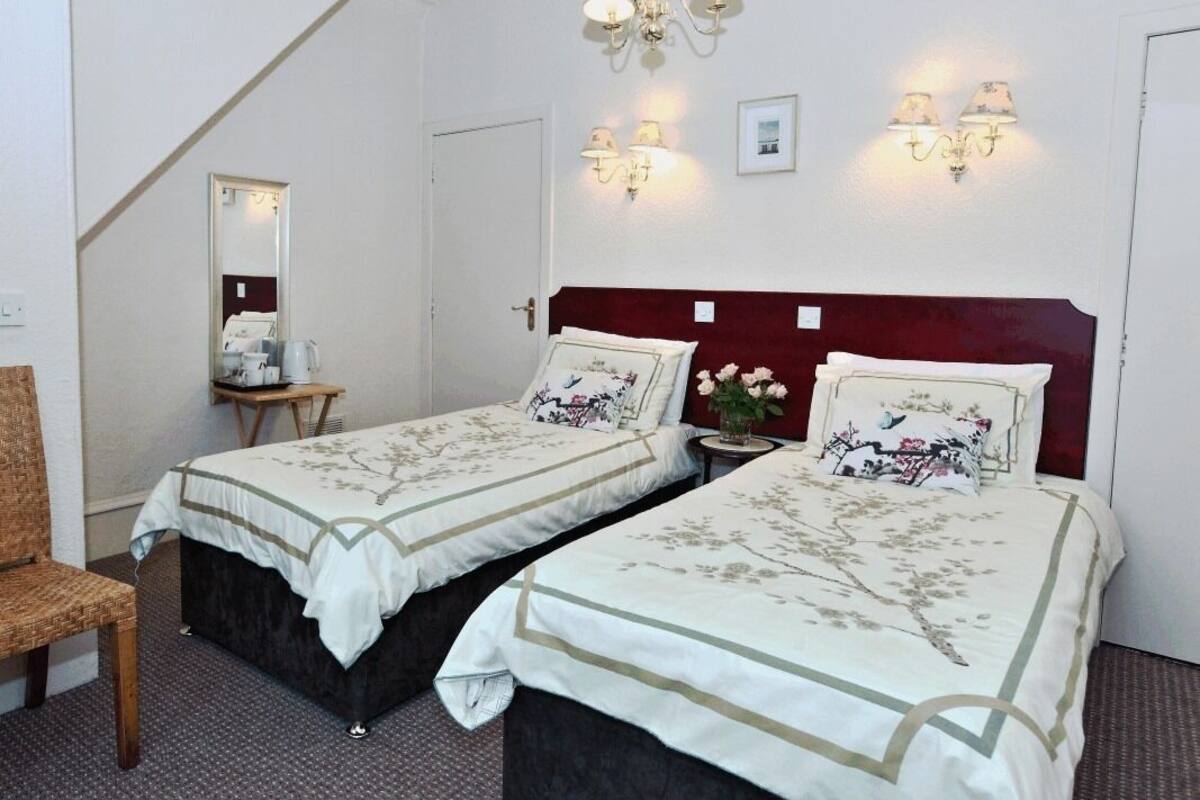 A hotel room with two beds, a chair, a small table, and a mirror.