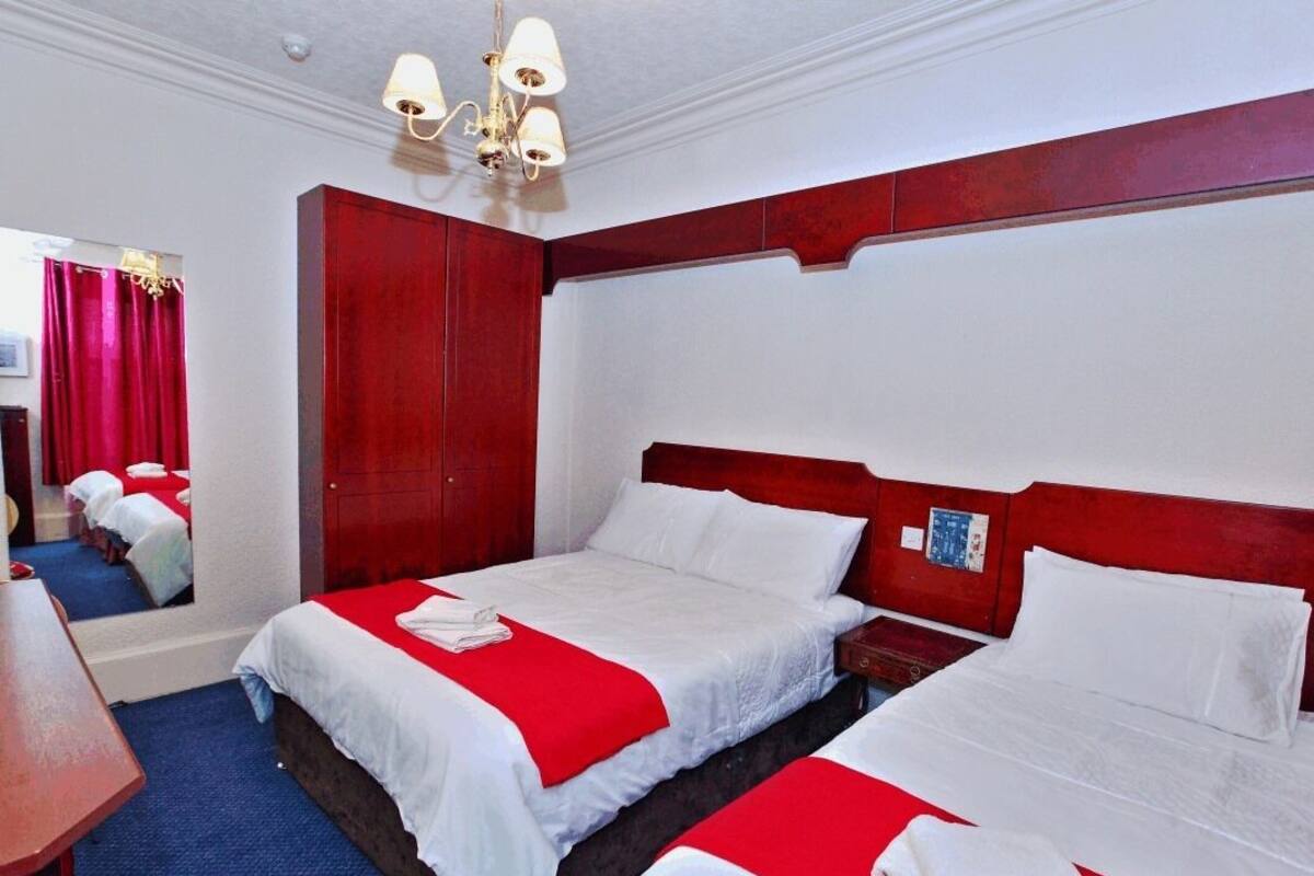 A hotel room with two beds, a wooden wardrobe, a mirror, and a chandelier.