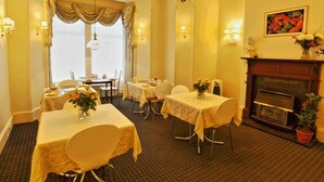 A dining area with tables set for four, a fireplace, and a chandelier. - Brentwood Villa Bed and Breakfast (Aberdeen)