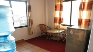 Cocina compacta con refrigerador, dispensador de agua, mesa de comedor con sillas y una ventana con cortinas.