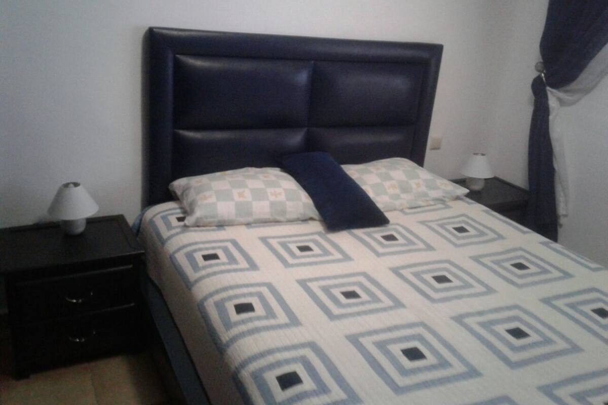 A bed with a geometric patterned bedspread, a dark headboard, and two bedside lamps on a nightstand.