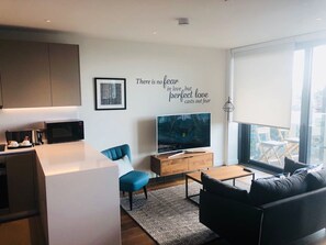 A modern living room with a flat-screen TV, a sofa, a coffee table, and a kitchen area with a microwave. - Exquisite Katryna (Wembley)