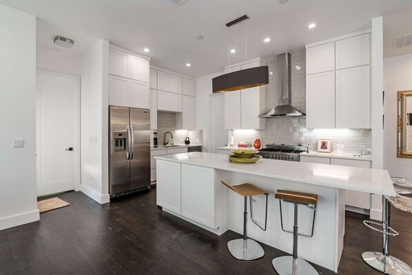 A modern kitchen with white cabinetry, stainless steel appliances, and a central island with bar stools.