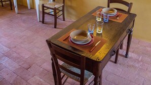 Un coin repas avec une table en bois dressée pour deux personnes, un bureau blanc avec un ordinateur et un luminaire fixé au mur.
